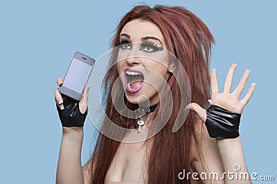 Portrait of funky young woman screaming while using cell phone over blue background