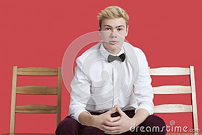 Portrait of a handsome young man in formal wear sitting on chair over red background
