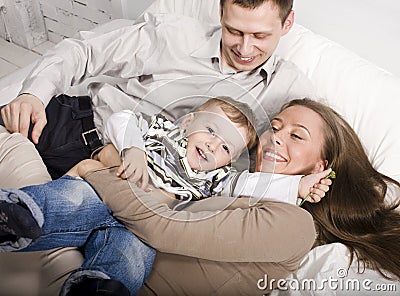 Portrait of happy family, mom and dad playing with their son in bed