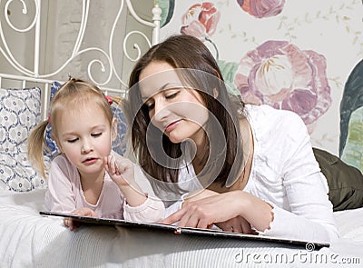 Portrait of happy family, mother and daughter in bed reading book