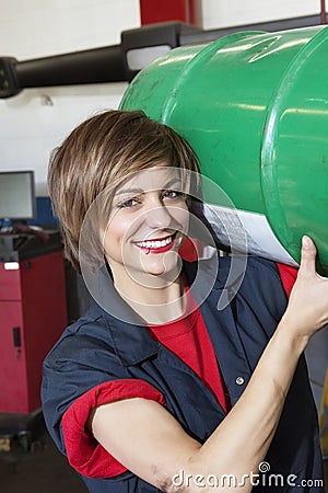 Portrait of a happy mechanic carrying oil drum in vehicle repair shop