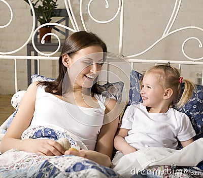 Portrait of happy mother and daughter in bed hugging and smiling