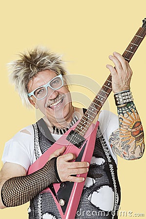 Portrait of happy senior male punk rock musician playing guitar over yellow background
