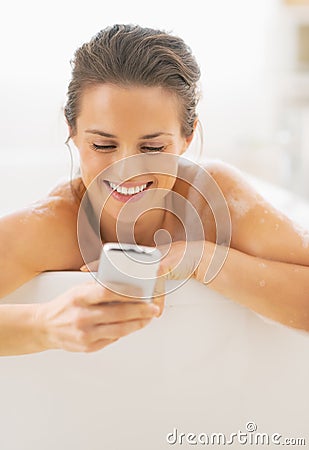 Portrait of happy young woman writing sms while in bathtub