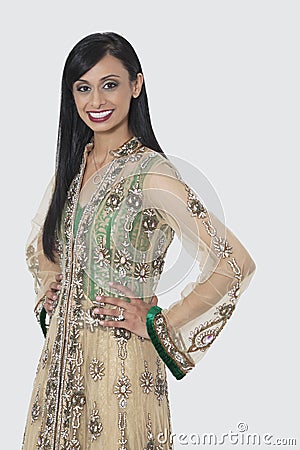 Portrait of an Indian woman in designer wear standing with hands on hips over gray background