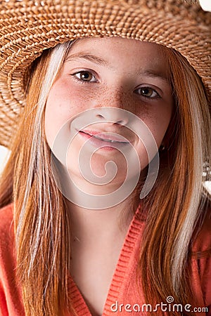 Portrait of little red-haired girl with freckles and a straw hat