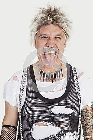 Portrait of senior male punk sticking out tongue over gray background