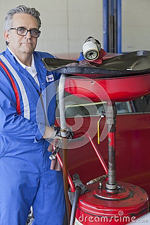 Portrait of senior mechanic standing besides car spray paint equipment