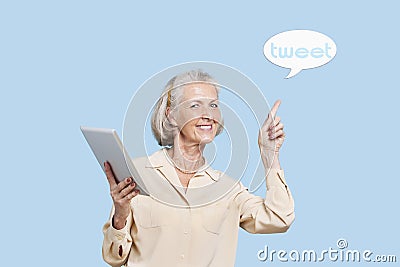 Portrait of senior woman with tablet PC pointing at tweet bubble against blue background