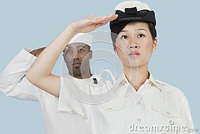 Portrait of serious female US Navy officer and male sailor saluting over light blue background