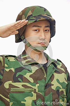 Portrait of serious young man in military uniform saluting, studio shot