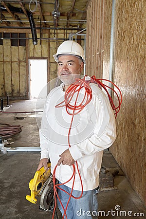 Portrait of a smiling male construction worker holding a power saw and a red electric wire