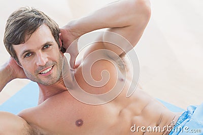 Portrait of a smiling shirtless young man doing sit ups
