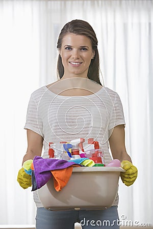 Portrait of smiling woman carrying basket of cleaning supplies at home