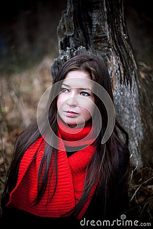 Portrait of woman in red scarf with long brunette hair in cold dark forest