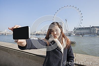 Portrait woman taking self portrait through cell phone against London Eye at London, England, UK