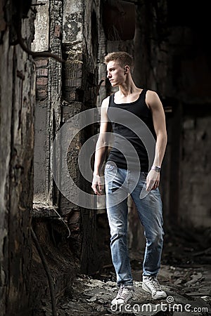 Portrait yog young man in shirt and jeans standing on abandoned background.