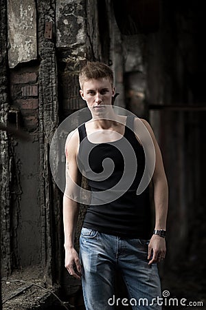 Portrait yog young man in shirt and jeans standing on abandoned background.