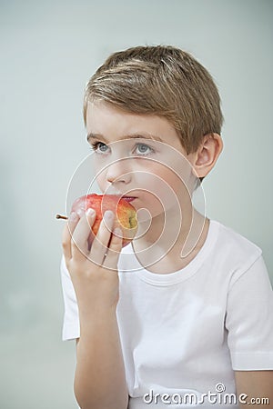 Portrait of young boy eating an apple over gray background