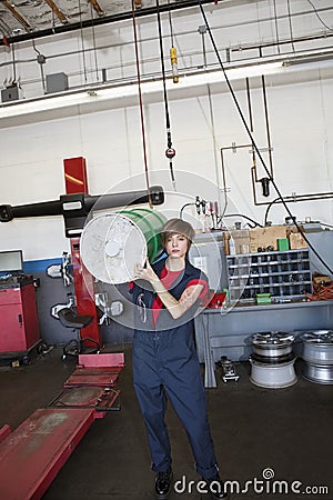 Portrait of a young female mechanic carrying oil drum on shoulder in auto repair garage