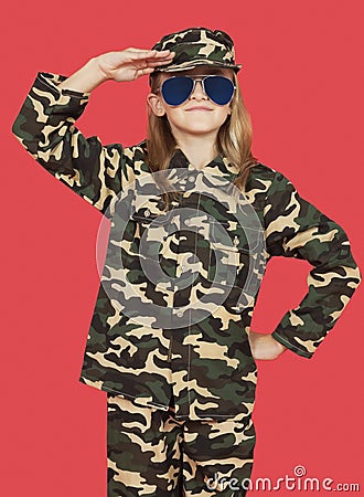 Portrait of young girl in military uniform saluting against red background