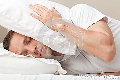 Portrait of Young man in bed hiding from noise