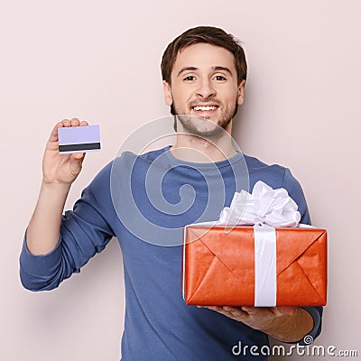 Portrait of young man holding gift box and a credit card. Handso