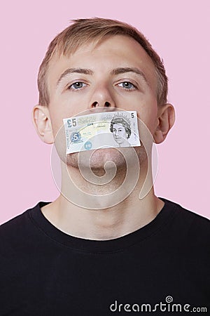 Portrait of a young man with paper money stuck over his mouth against pink background