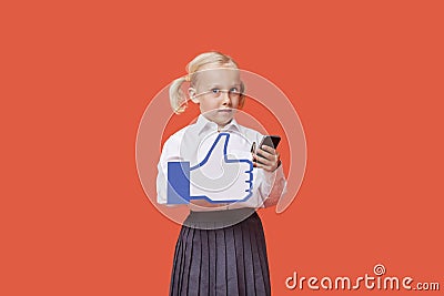 Portrait of a young schoolgirl with cell phone holding fake like button over orange background