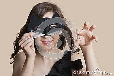 Portrait of a young woman looking through eye mask imitating as cat over colored background