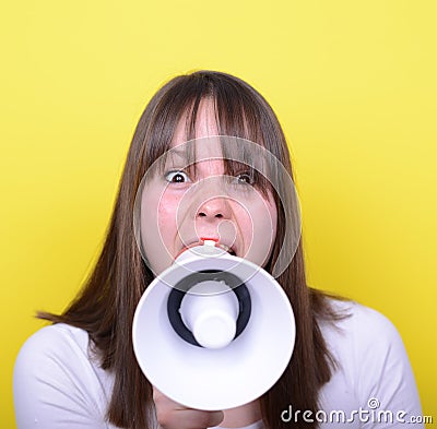 Portrait of young woman shouting with a megaphone against yellow