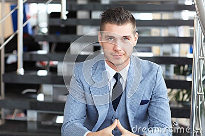 Positive business man sitting on stairs of modern office