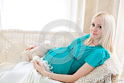 Pregnant blonde woman relaxing on sofa, reading book, dreaming,