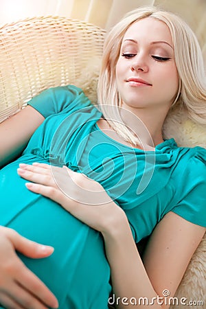 Pregnant blonde woman relaxing on sofa, reading book, dreaming,