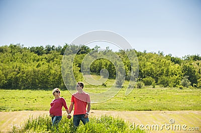 Pregnant couple standing in front of a field and wood.