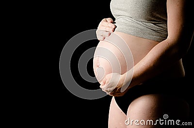 Pregnant woman on black background with hands on her belly