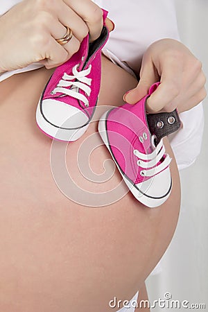 Pregnant woman holding shoes for newborns