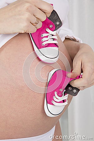 Pregnant woman holding shoes for newborns