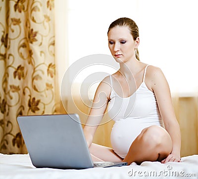 Pregnant woman relaxing with her laptop on a bed