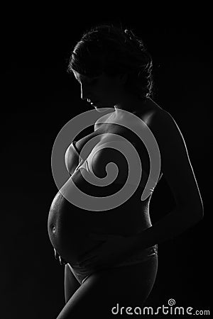Pregnant woman silhouette over black background. Side view.