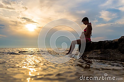 Pregnant woman sitting on a rock by the sea