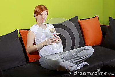 Pregnant woman sitting on sofa with teddy bear