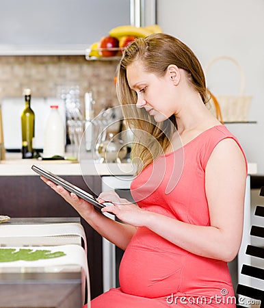 Pregnant woman using a tablet computer in kitchen