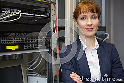 Pretty computer technician smiling at camera beside server