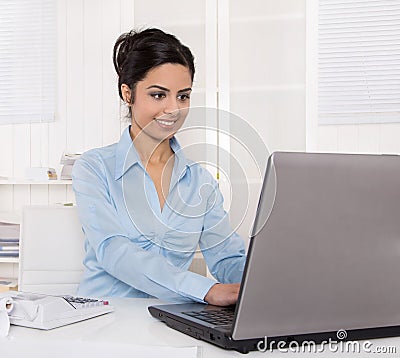 Pretty young indian businesswoman sitting at desk writing a mess