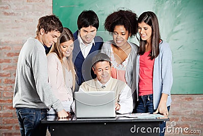 Professor And Students Looking At Laptop In