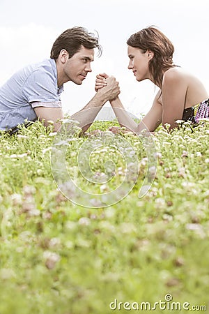 Profile shot of couple arm wrestling while lying on grass against sky