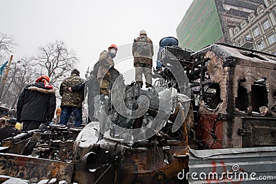 Protesters with hidden faces guard on the top of burned and smashed buses on winter street during anti-government protest