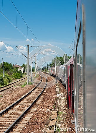 Railway and train go to horizon in green landscape under blue sky with white clouds