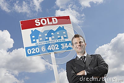 Real Estate Agent In Front Of Sold Sign And Cloudy Sky